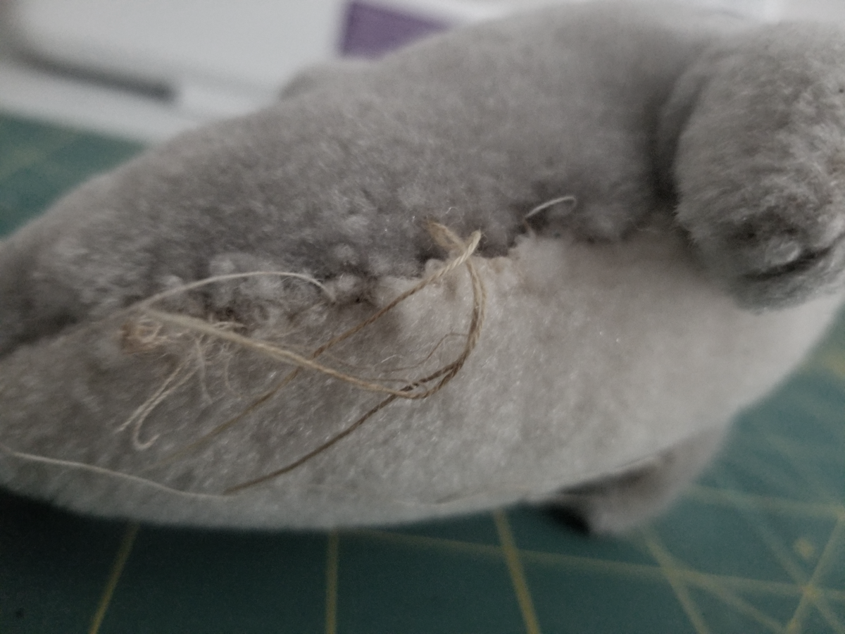 The stitches on the side of the dolphin are old, brown, and fraying.